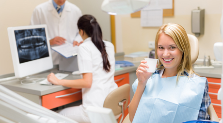 Woman sitting in dentist chair holding up cup.